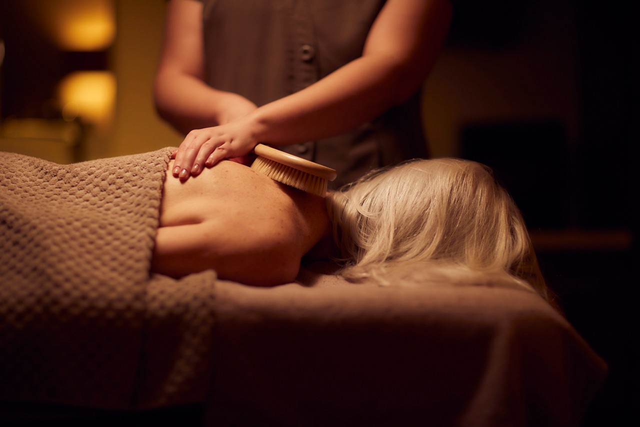 Spa therapist giving a woman a body brush treatment.